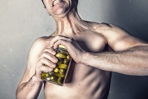 A man with no shirt trying unsuccessfully to open a can of pickles