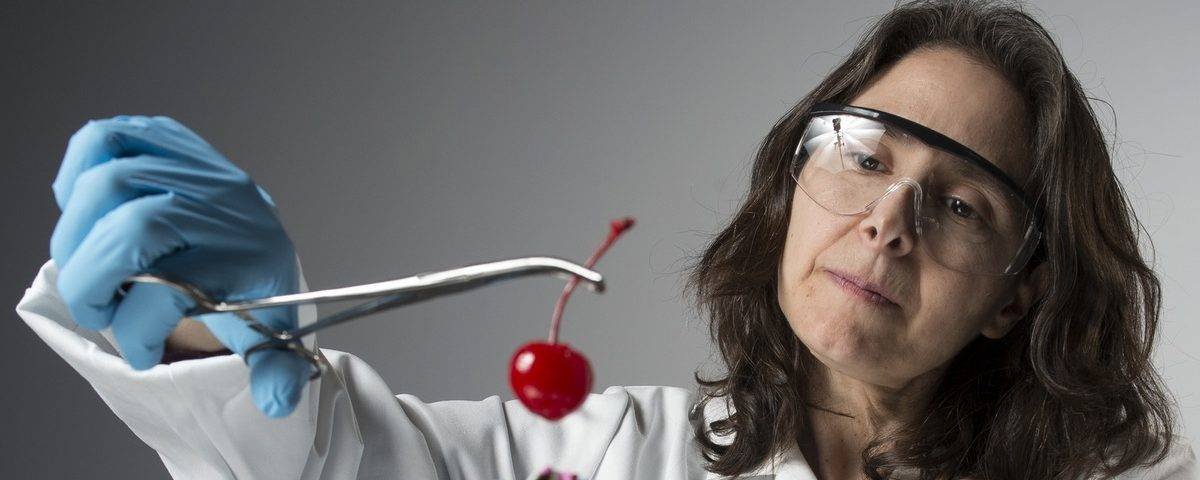 Image of Traci Mann in a lab coat holding a cherry with forceps over a bowl of ice cream