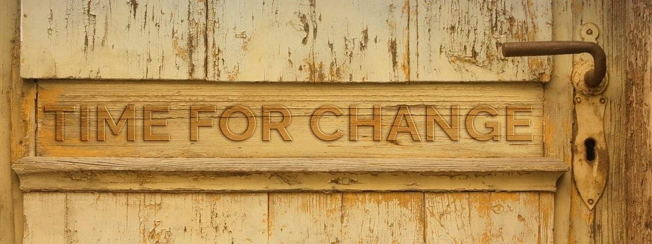 Image of a sign on a worn beige colored door that reads Time For Change